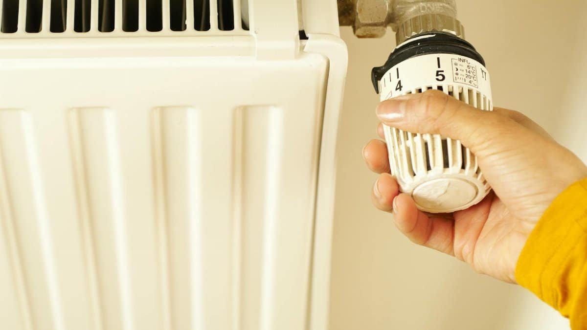 Close-up of hand adjusting radiator thermostat to control home heating temperature.