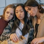 Three young women consoling each other while sharing popcorn indoors, signifying friendship and support.