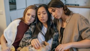 Three young women consoling each other while sharing popcorn indoors, signifying friendship and support.