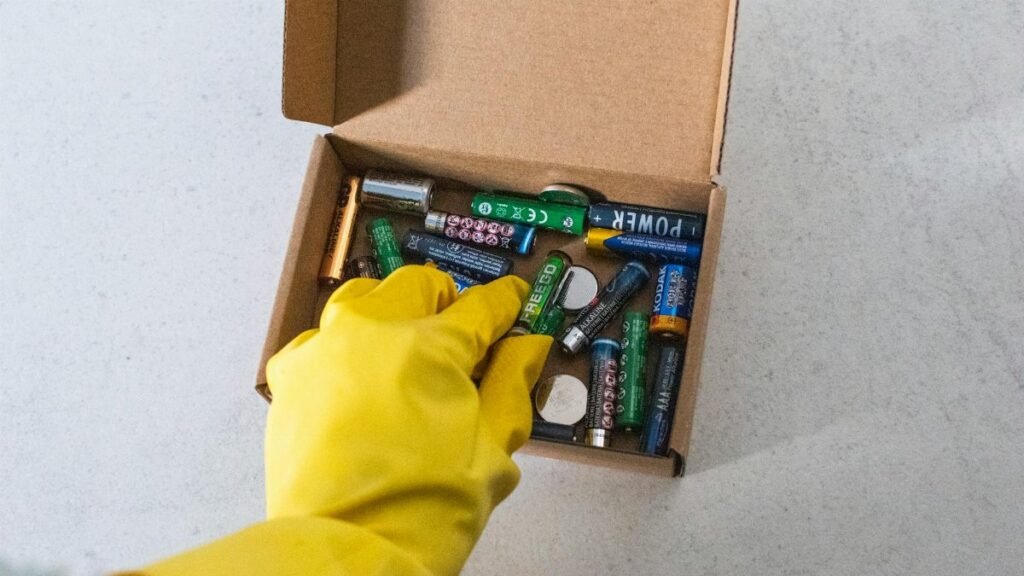 Yellow-gloved hand handling used batteries for safe recycling.