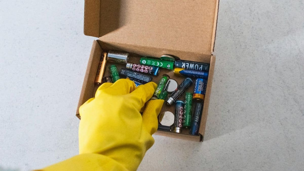 Yellow-gloved hand handling used batteries for safe recycling.