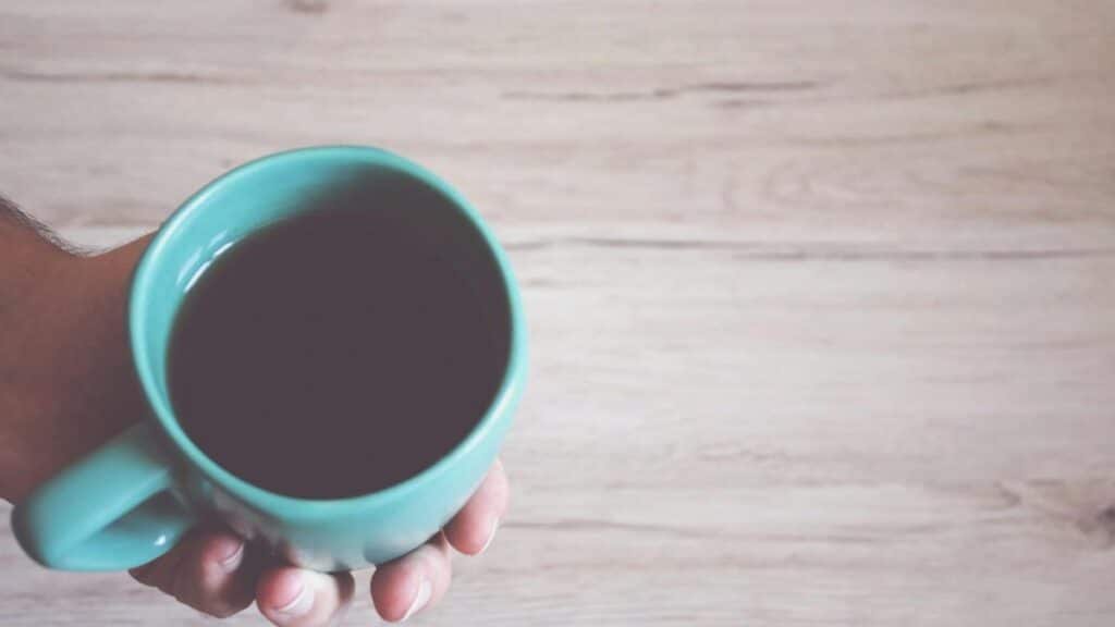 A close-up view of a hand holding a coffee mug on a wooden table, conveying a warm morning atmosphere.