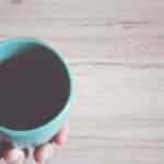 A close-up view of a hand holding a coffee mug on a wooden table, conveying a warm morning atmosphere.