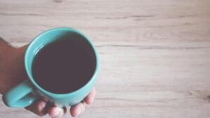 A close-up view of a hand holding a coffee mug on a wooden table, conveying a warm morning atmosphere.