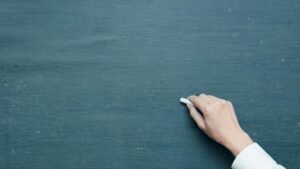 Hand holding chalk ready to write on a blank blackboard surface.