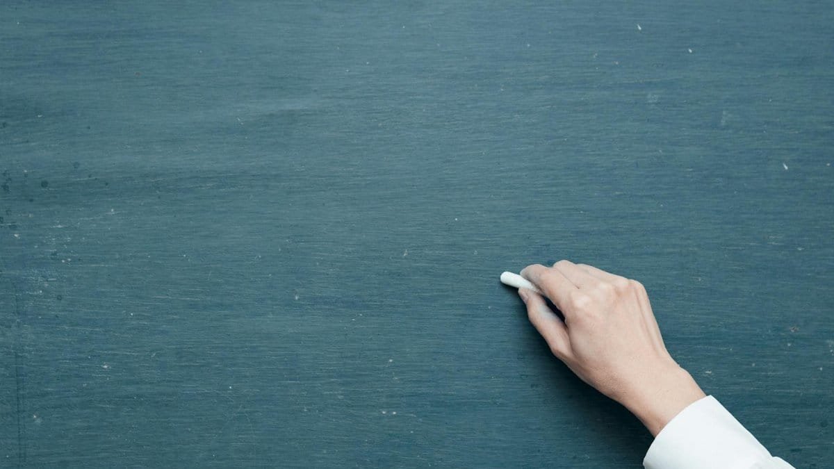 Hand holding chalk ready to write on a blank blackboard surface.