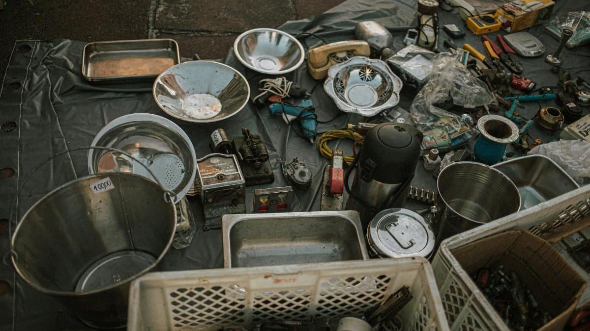 Assorted metal items and vintage tools displayed at an outdoor flea market on asphalt.