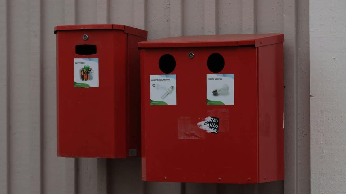 Two red recycling bins for batteries and light bulbs mounted on urban wall.