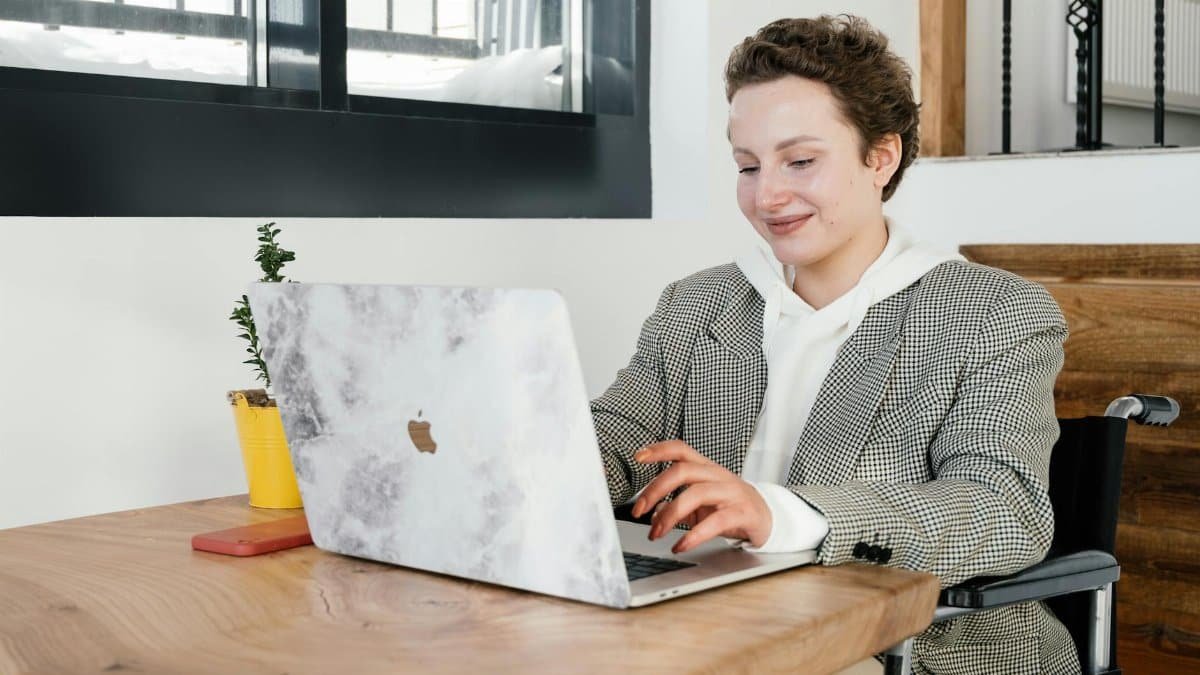 Woman in wheelchair typing on laptop at a café, embodying modern remote work and independence.