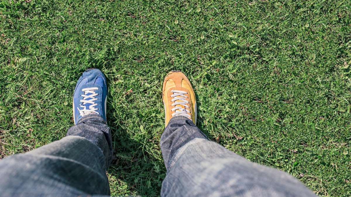 A person wearing mismatched shoes stands on green grass, highlighting differences and individuality.