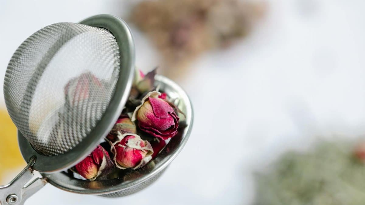 Delicate dried rosebuds in a mesh tea infuser, perfect for herbal teas.
