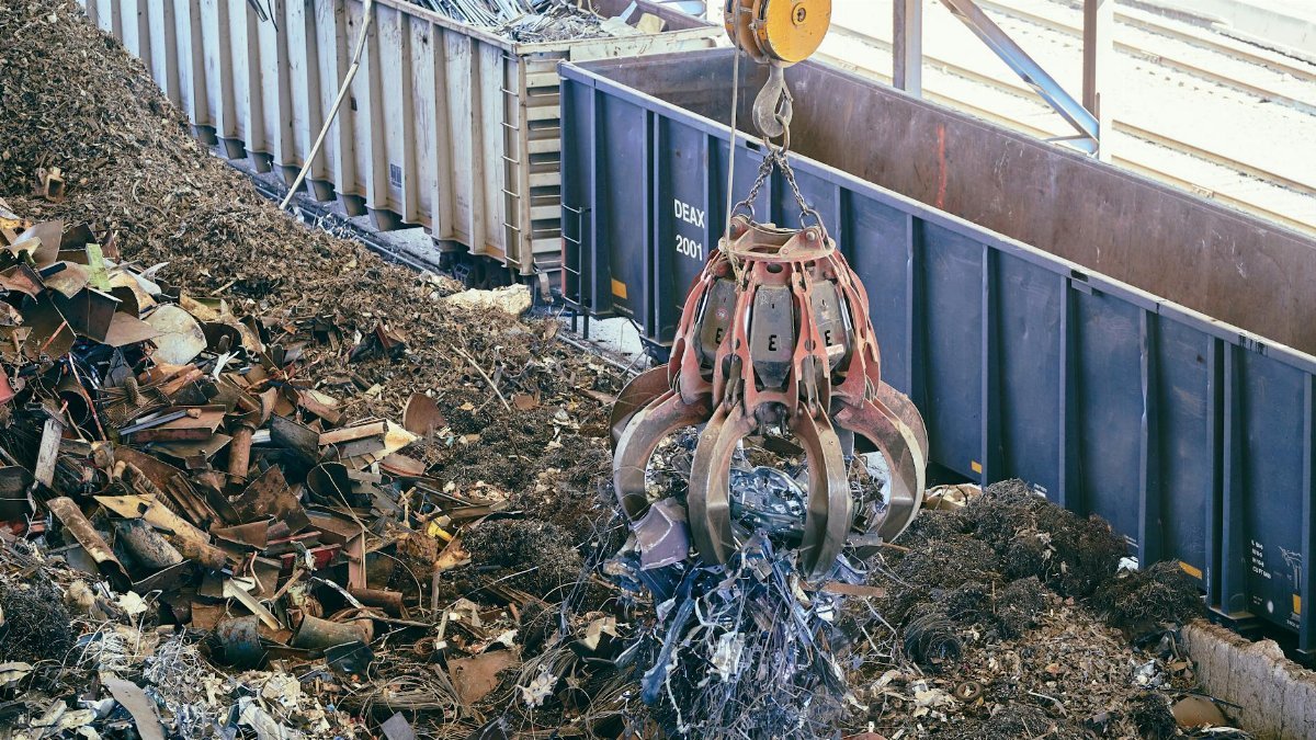 A claw crane lifting scrap metal in an industrial recycling facility.
