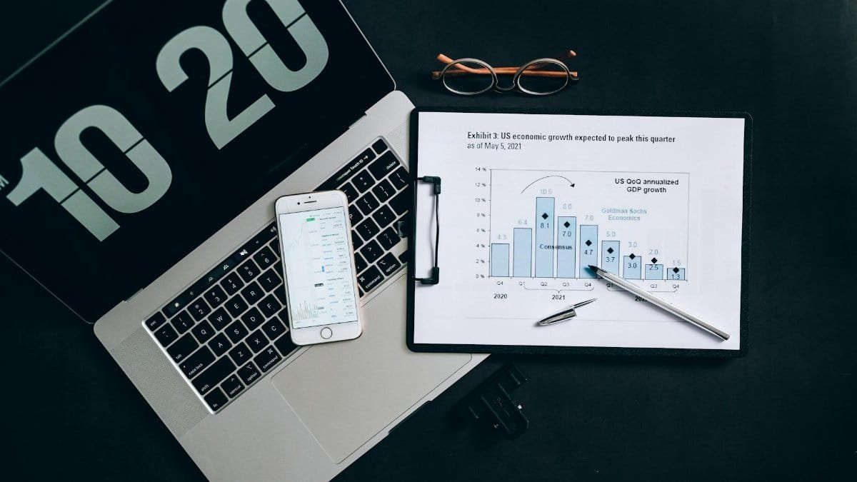 Top view of financial analysis tools on a desk including a laptop, smartphone, and graphs.