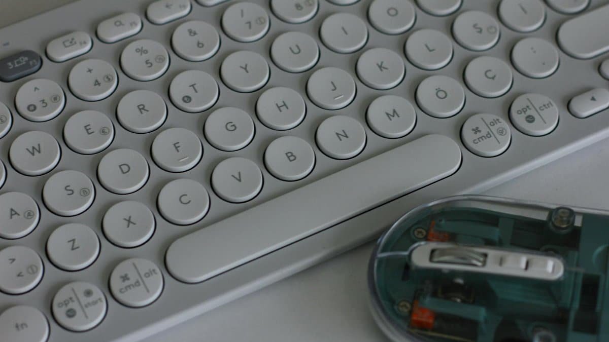 Ergonomic wireless keyboard and transparent mouse on a white desk, sleek and modern design.