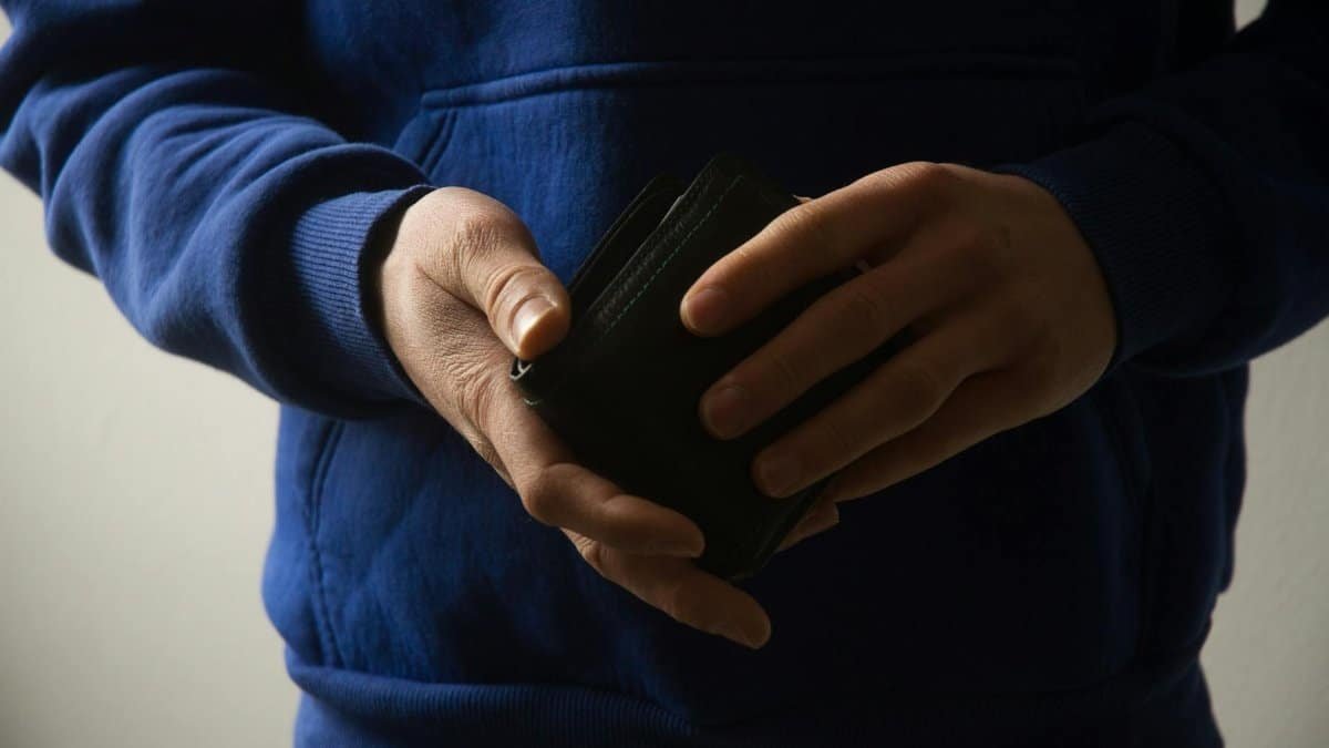 Close-up of a man holding a wallet, showcasing casual menswear style in a blue hoodie.