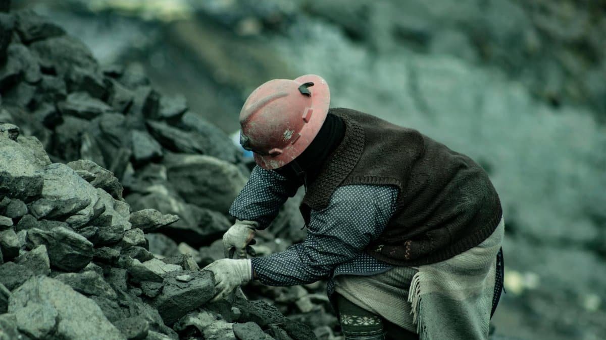 A coal miner in a hard hat working amidst rocky terrain, emphasizing labor and resilience.