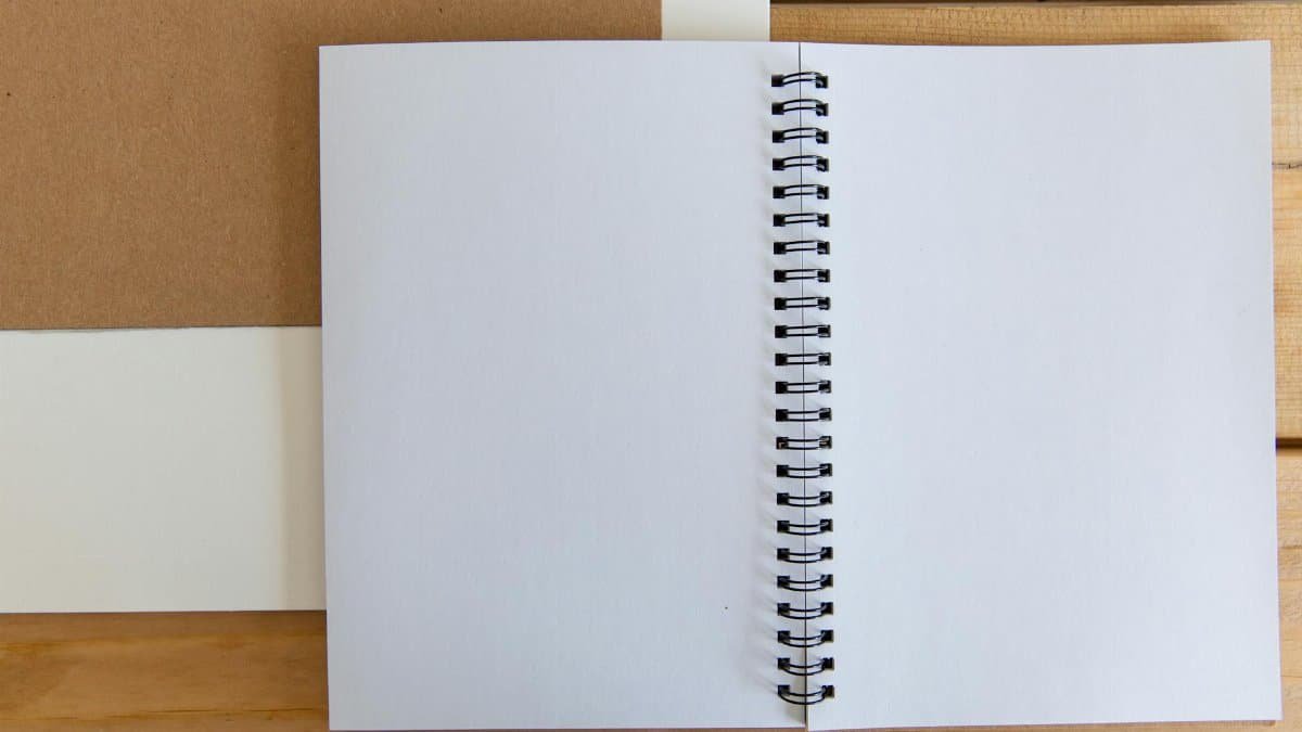 Open white spiral notebook on a wooden desk for simple and minimalist design projects.