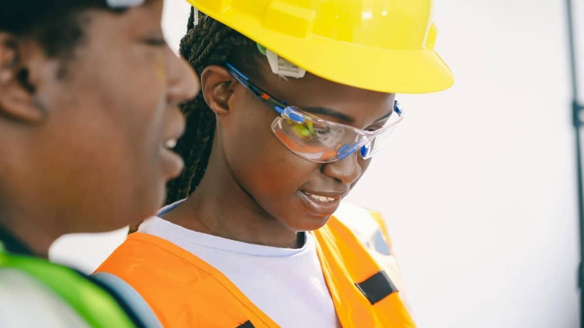 Two women engineers on site with hard hats and safety vests focusing on a task.