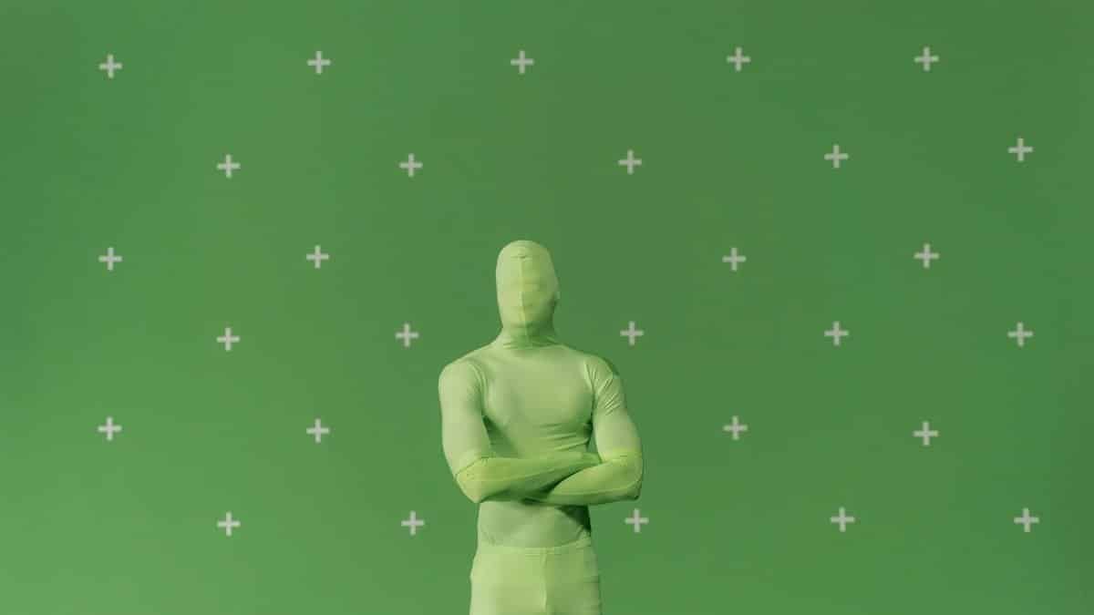 Person in a green chroma key suit standing against a marked green screen in a studio.
