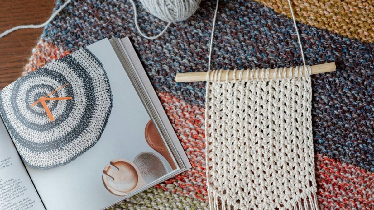 Top view of composition of white macrame decor near colorful magazine and knitting ball on table