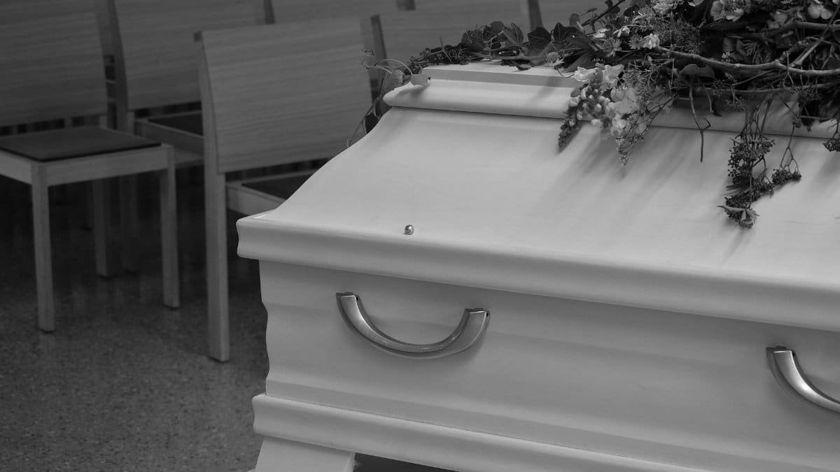 Grayscale image showing a coffin with flowers in a funeral setup, capturing sorrowful atmosphere.