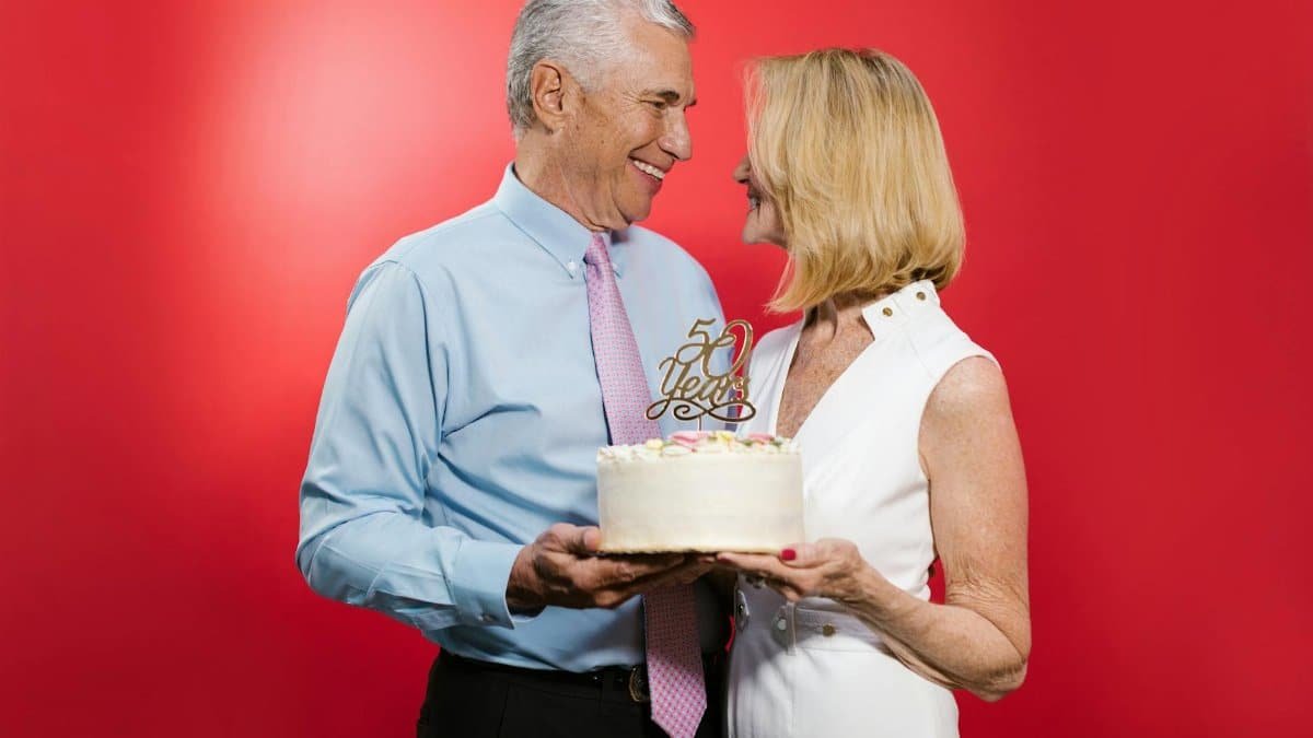 Happy senior couple celebrating their 50th anniversary with cake in a studio setting.