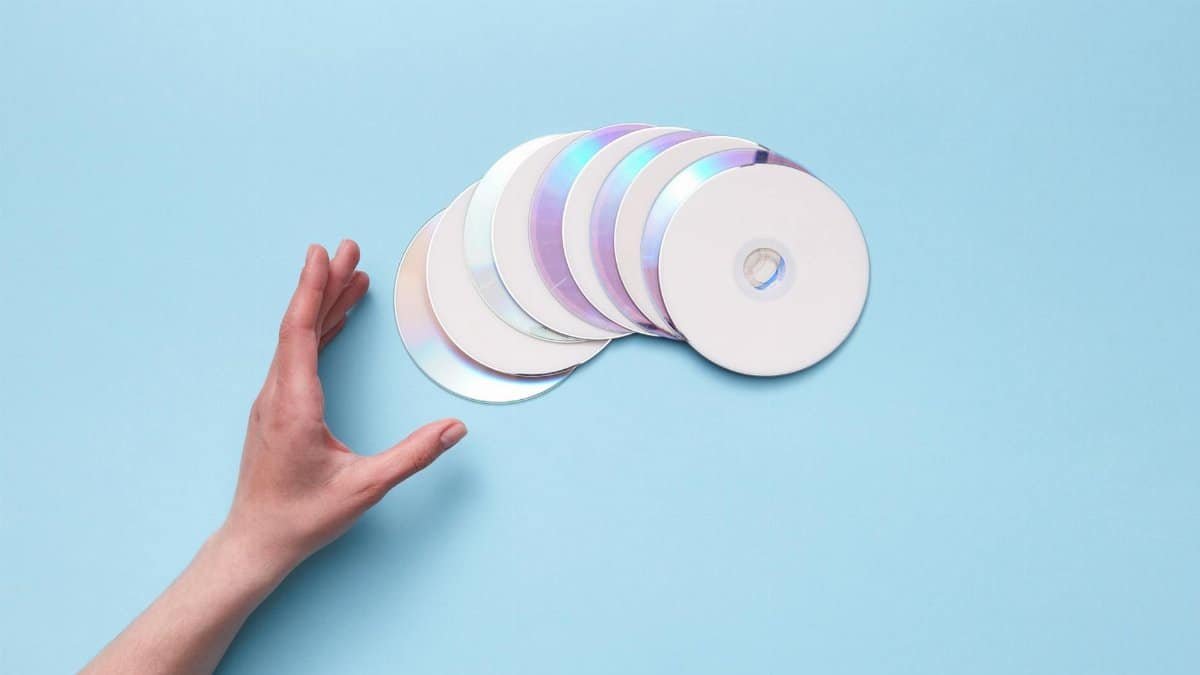 A hand reaching out to a stack of CDs on a blue backdrop, evoking nostalgia for retro technology.
