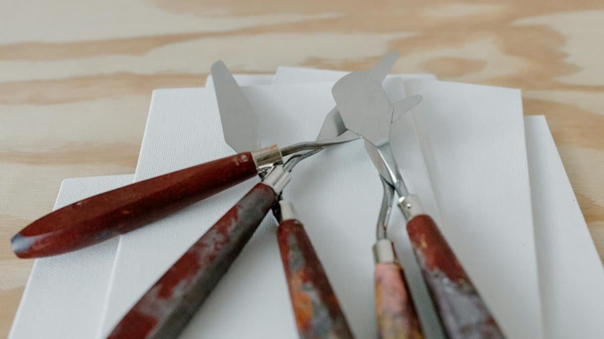 A set of palette knives rests on a blank canvas, ready for painting inspiration.