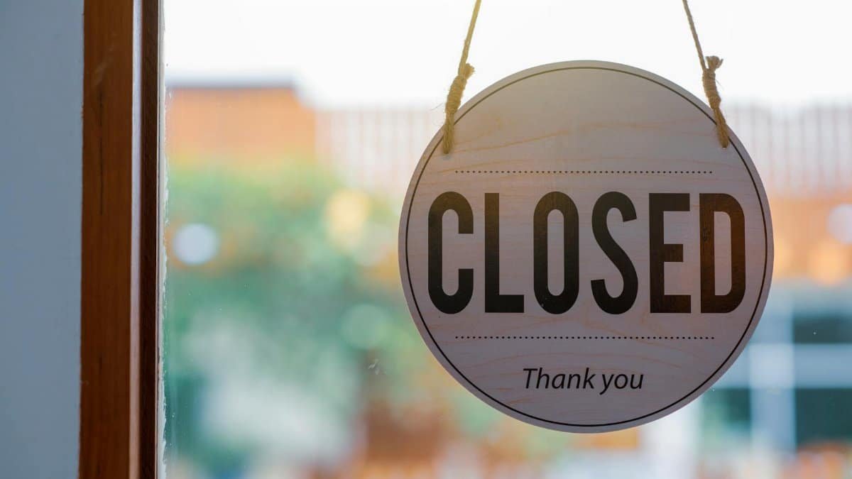 Wooden closed sign hanging on a shop window, with blurred background outside.
