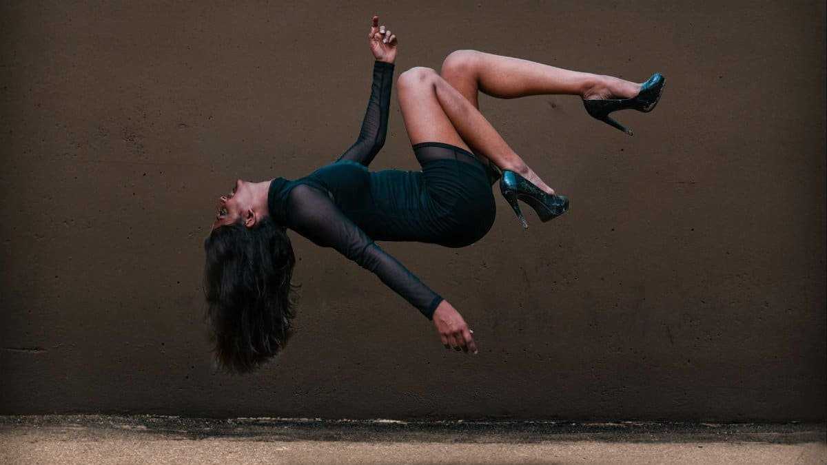 A woman in levitation pose against a textured wall, wearing an elegant dress.