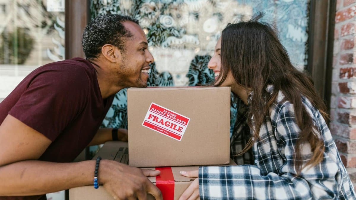 A joyful couple enjoying the moving day experience while carrying boxes labeled 'Fragile'.