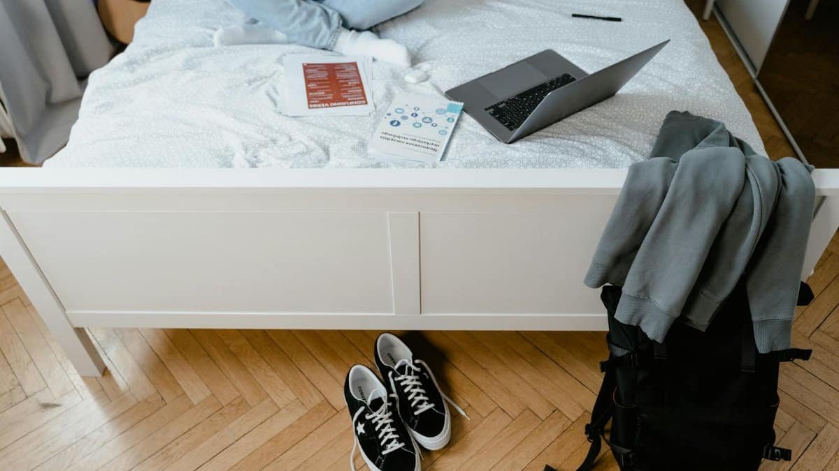 A laptop, books, and casual clothing on a bed create a relaxed remote work environment.