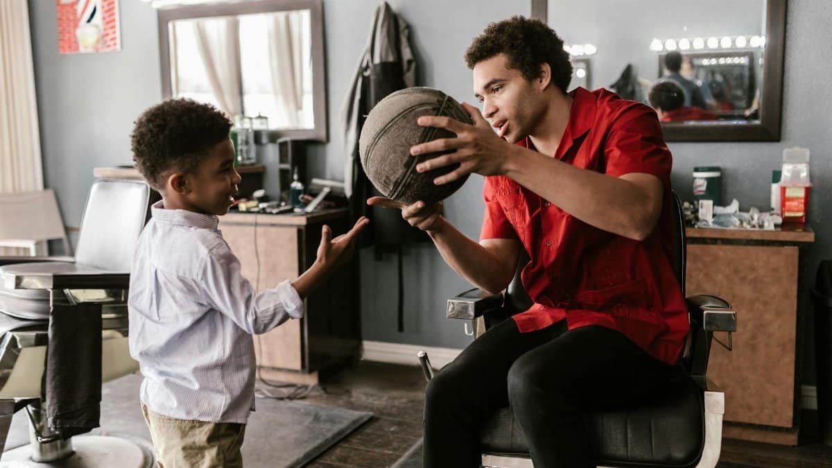 A young boy receives a basketball lesson from an adult in a barbershop setting.