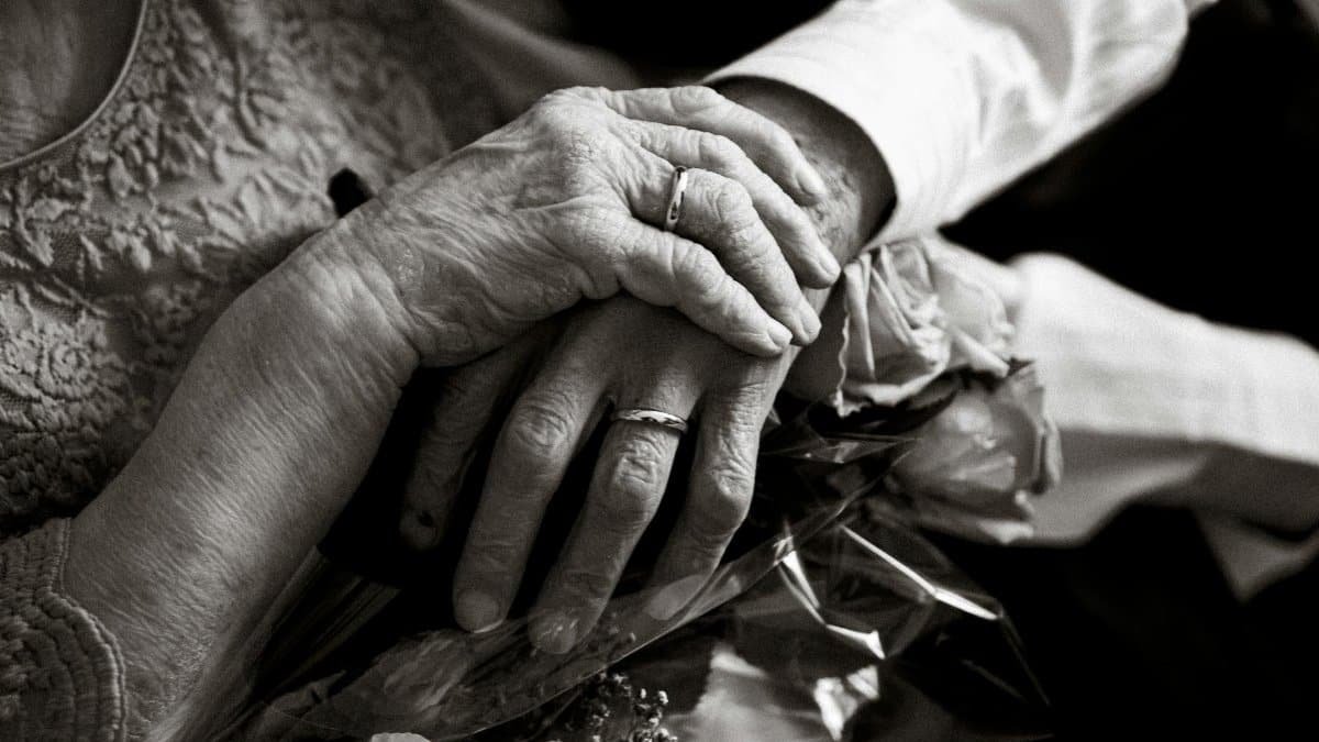 Black and white photo of an elderly couple holding hands with wedding rings, symbolizing love and companionship.
