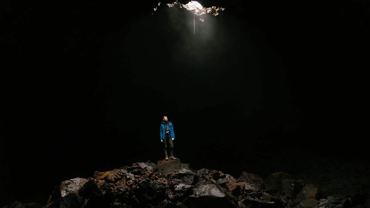 Man standing in a dark cave under a natural light beam, showcasing adventure and mystery.