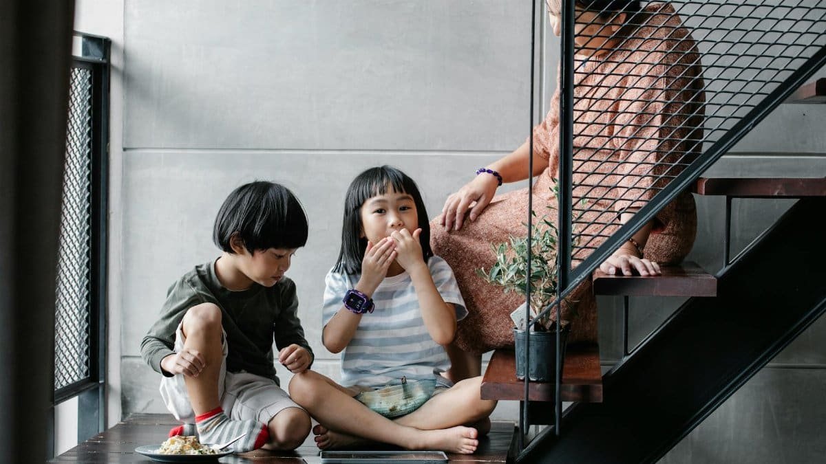 Children enjoying snacks with a relative on a cozy indoor staircase.
