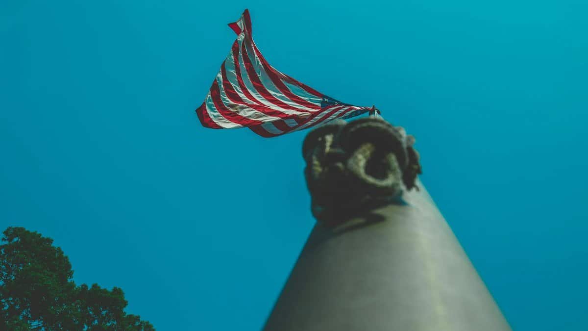 Upward perspective of the American flag on a flagpole against a clear blue sky.