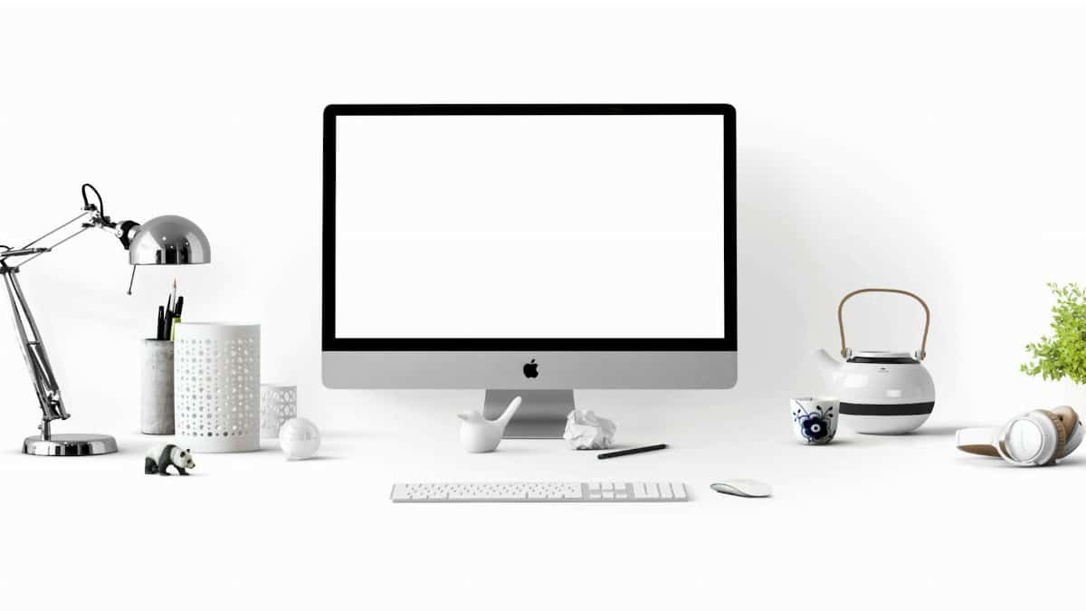 Minimalist office desk with an iMac, lamp, and stationary, perfect for tech backgrounds.