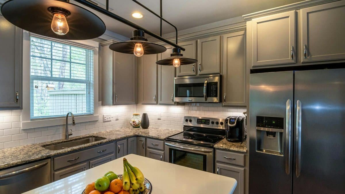 Contemporary kitchen featuring a bowl of fruits, stainless appliances, and elegant lighting.