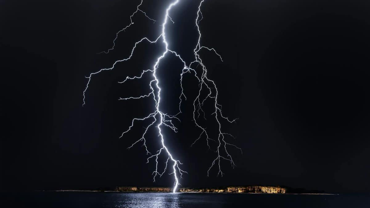 Dramatic lightning bolt over the ocean at night, illuminating the coastal landscape.
