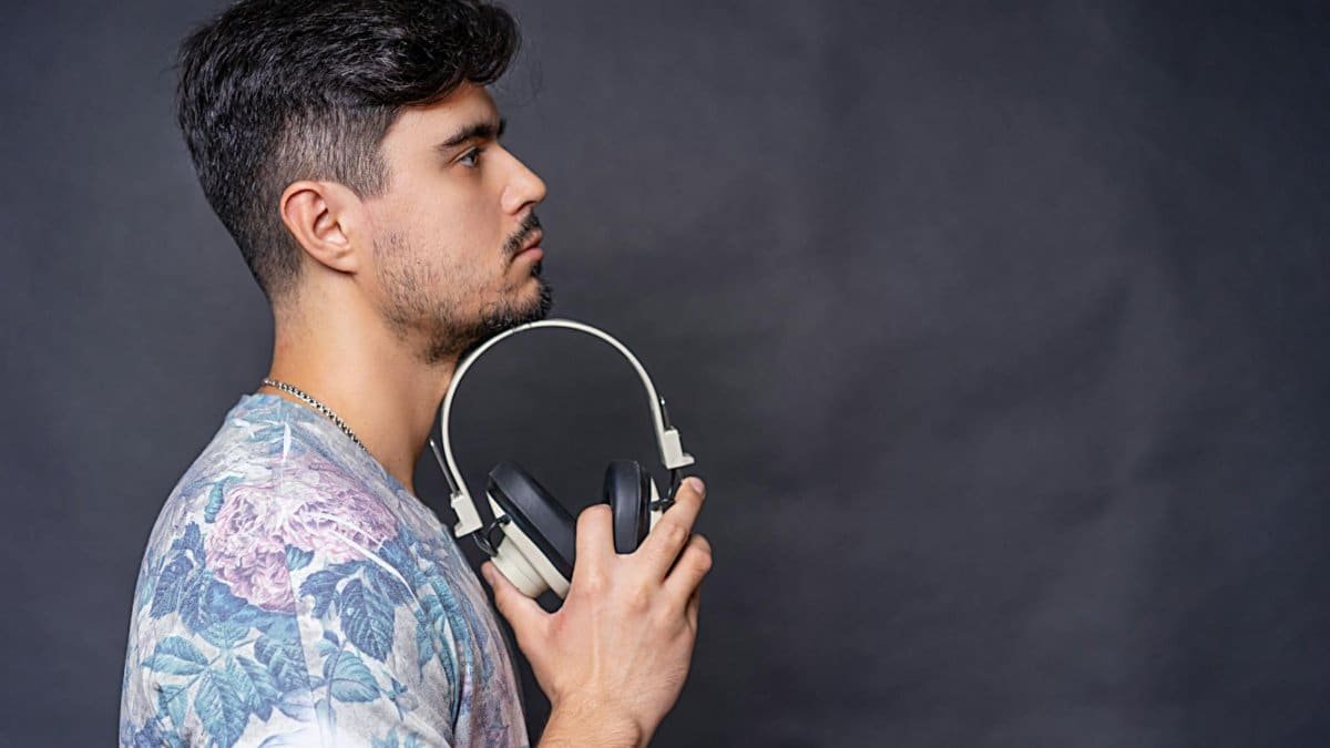 Side view portrait of a man holding headphones in a studio setting against a dark background.