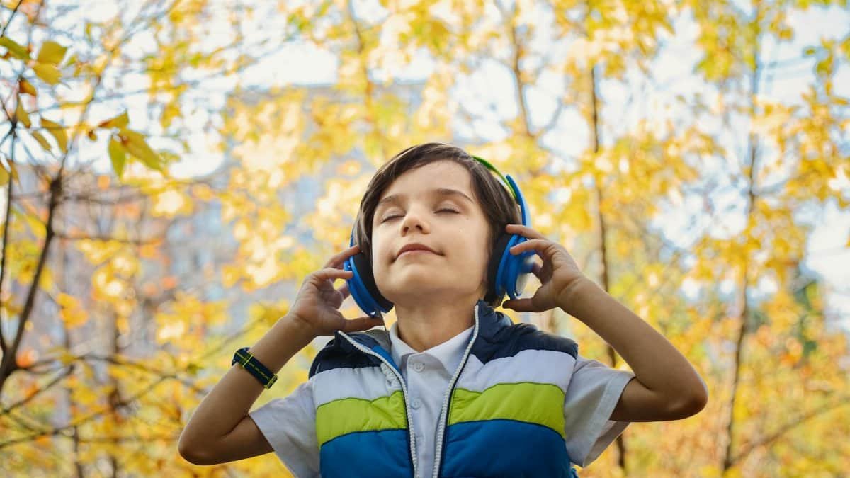 A young boy enjoys music through headphones amidst colorful fall foliage.