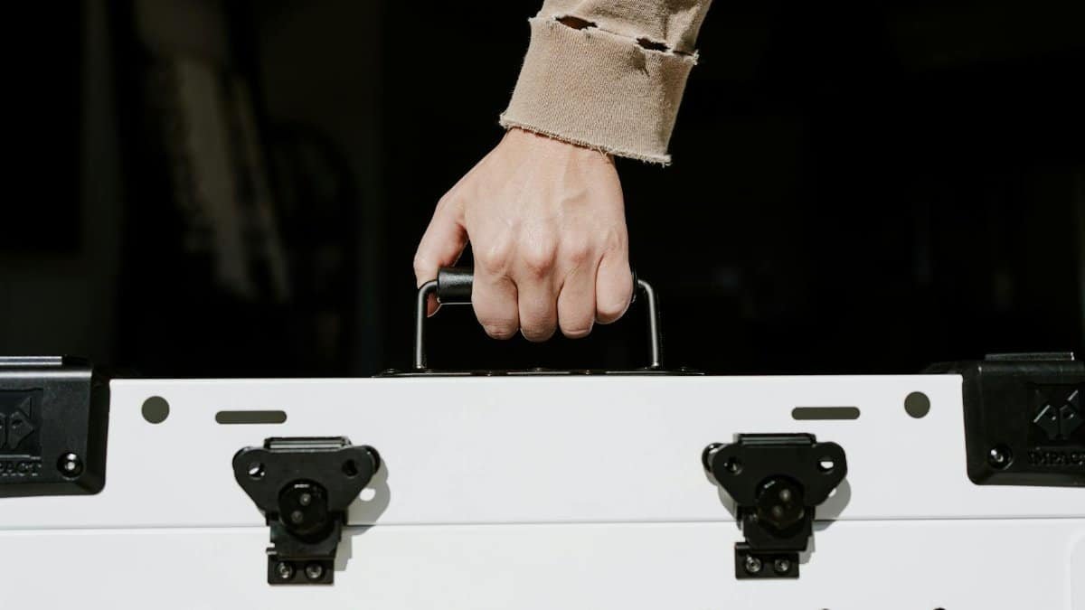 A hand holding the handle of a durable white dog crate indoors.