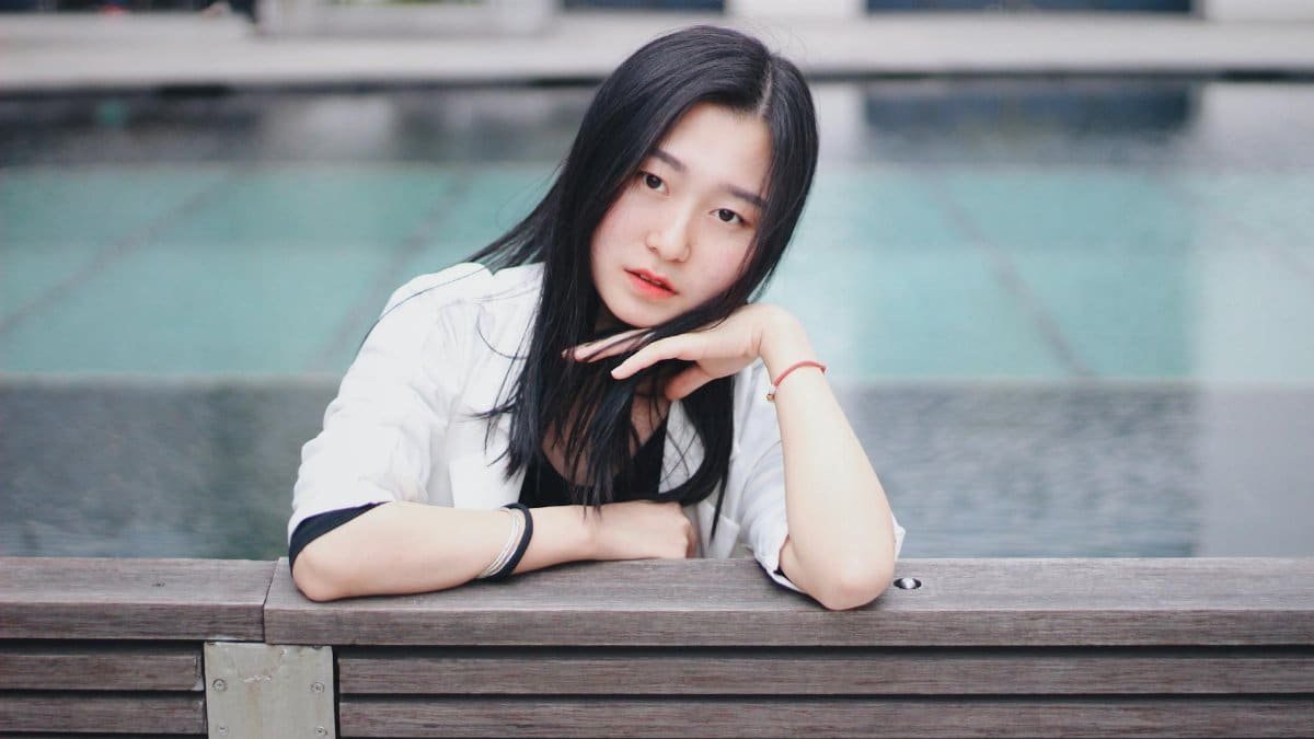 A fashionable woman posing elegantly on a bench beside a pool, showcasing modern style.