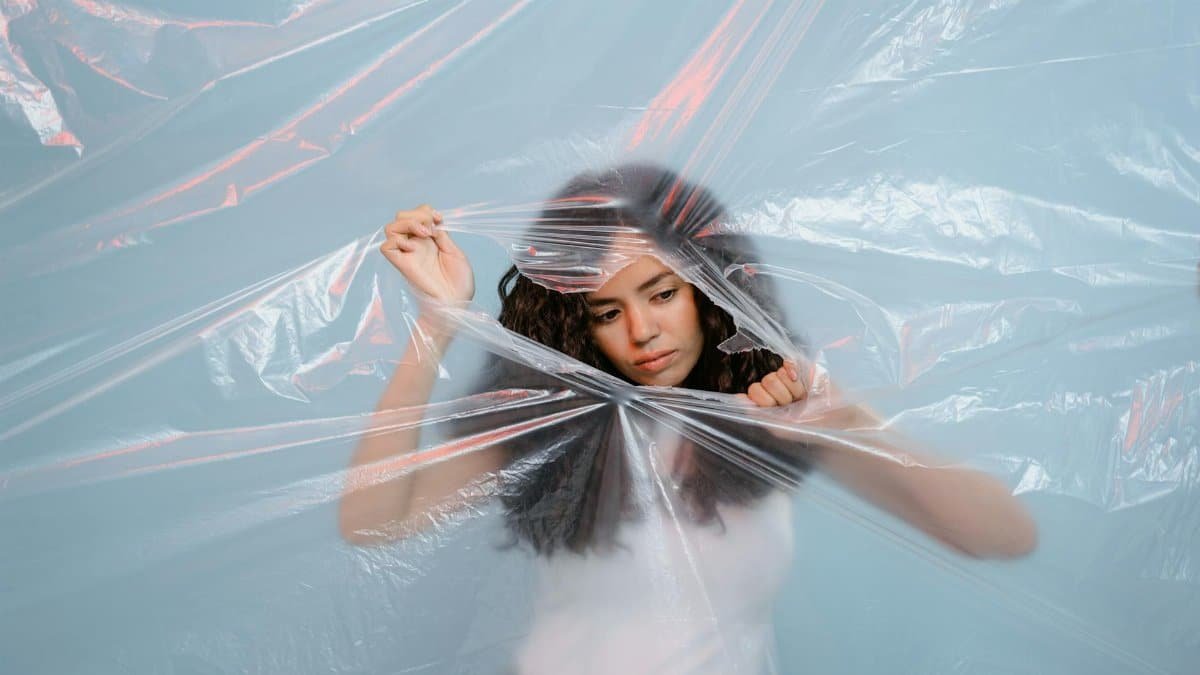 A young woman pushing against a plastic sheet, symbolizing environmental awareness and zero waste.