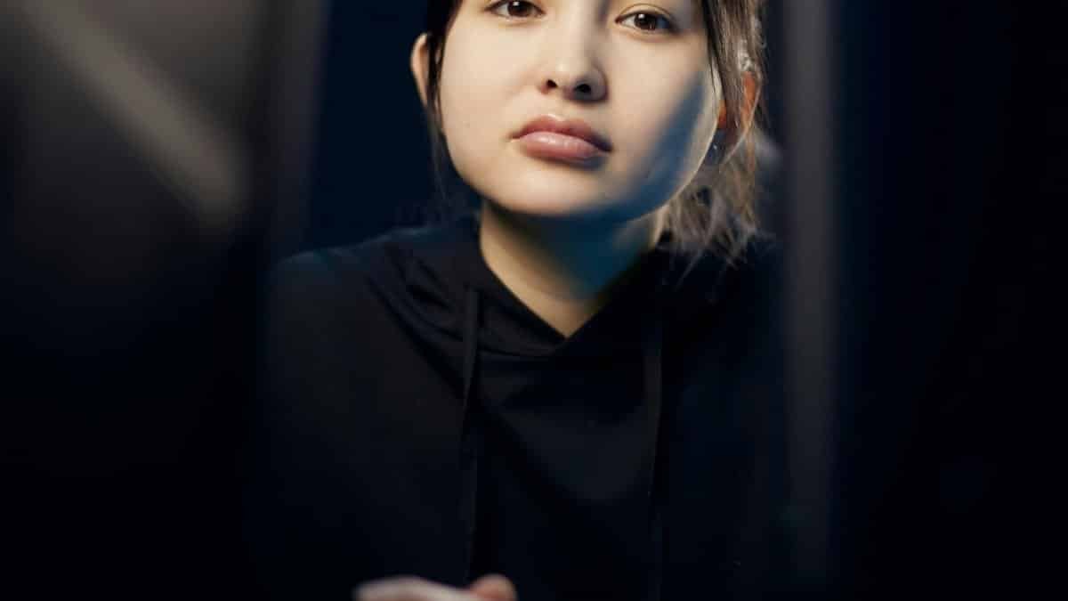 Close-up of a thoughtful young woman in a black hoodie, looking ahead with clasped hands.