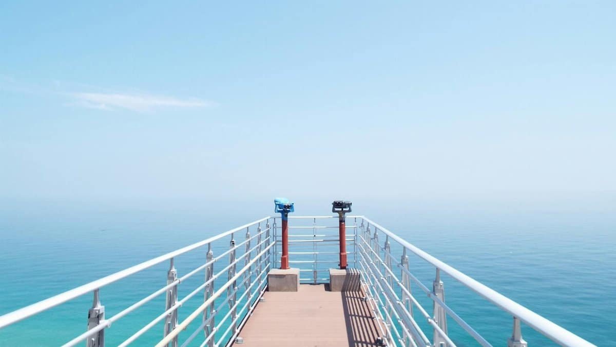 Experience the serenity of a sunny day on a coastal pier overlooking the tranquil sea.