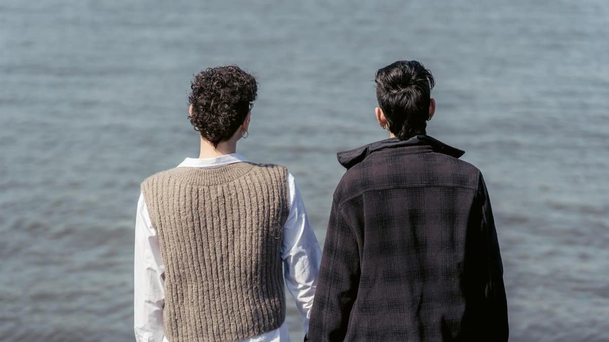 Back view of unrecognizable best friends in warm clothes admiring rippling water of river