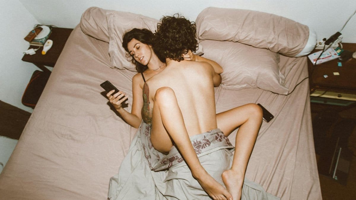 A couple in bed looking at smartphones, highlighting modern disconnection.