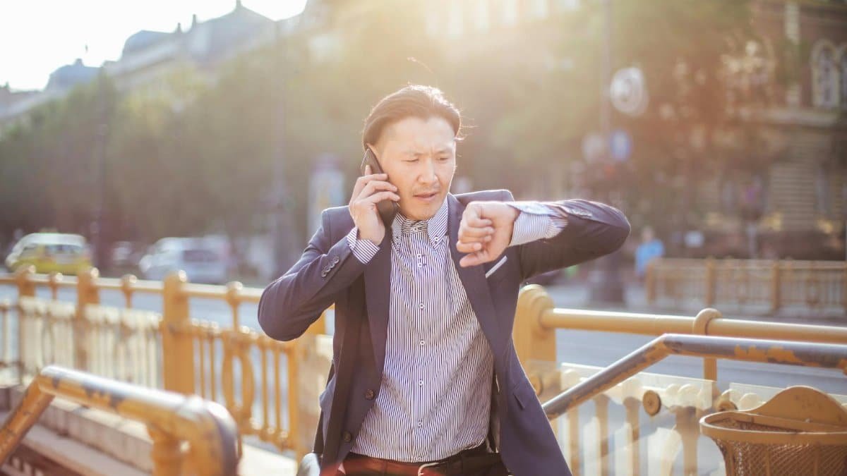 Asian businessman in suit checking time while on phone outdoors.